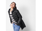 Woman in black quilted jacket, striped sweater, and blue jeans, smiling.