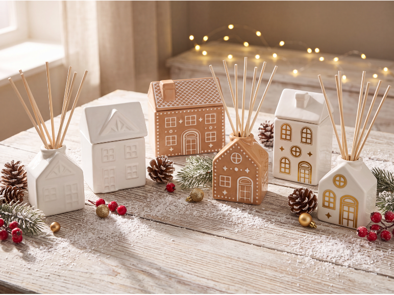 Christmas ceramic diffusers and jars shaped like houses on a wooden table.