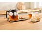 Glass teapot with tea and cookies on a wooden kitchen countertop.