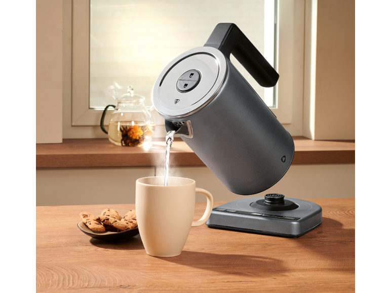 Electric kettle pouring hot water into a mug, with cookies and a teapot.