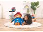 Girl playing with a large and small teddy bear, wearing blue coats and red hats.