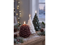 Three lit LED candles shaped like Christmas trees and a pinecone on a snowy wooden table.