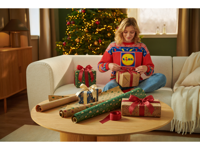 Woman in a Christmas sweater wrapping gifts in front of a Christmas tree.
