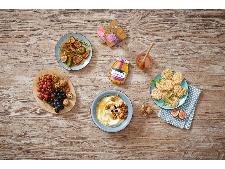 Honey, yogurt with nuts, figs, sesame cookies, and dried fruit on wood.