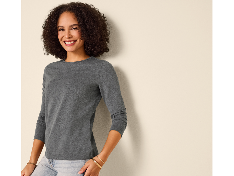 Smiling woman in a gray long-sleeve shirt and light jeans.