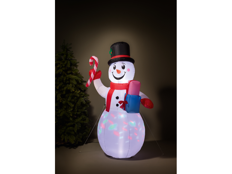 Inflatable snowman with a top hat, scarf, candy cane, and gift, next to a Christmas tree.