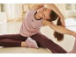 Woman in a pink tank top and burgundy leggings stretching on the floor.