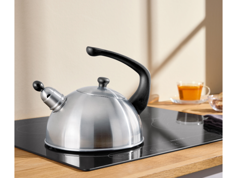 Stainless steel kettle on an induction hob with a cup of tea in the background.