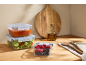 Glass food containers with salad, sauce, and berries on a wooden countertop