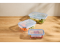 Three glass containers with blue lids, filled with vegetables and pasta, on a wooden table.