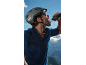 Cyclist in helmet and jersey drinking from a water bottle, with mountains in the background.