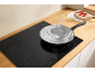 Frying pan with splatter guard on an induction hob in a kitchen with a wooden countertop.