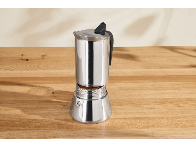 Open stainless steel moka pot with coffee on a wooden table