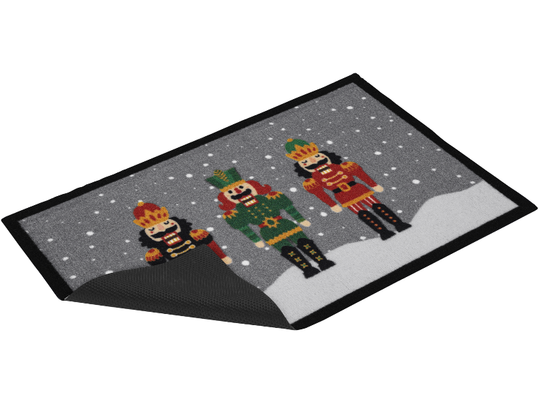 Christmas doormat with three nutcrackers, one black, one green, and one red, on a snowy background.