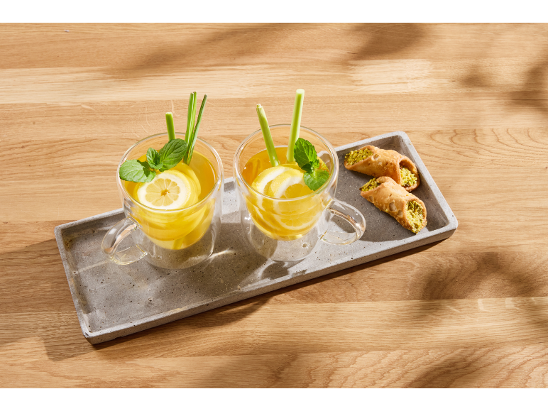 Two glasses of lemon and mint tea with lemongrass, served with pistachio cannoli on a tray.