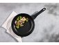 Black frying pan with salmon, broccoli, and red onion on a grey background.