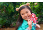 Smiling girl in a bear ear headband holding a pink doll and a small animal figure.