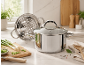 Stainless steel pot with lid and steamer insert in a kitchen setting.