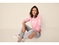 Smiling woman in pink snowflake-patterned sweater and light jeans, sitting on the floor.
