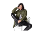 Woman in green puffer jacket, grey sweater, and black leather pants sitting on a chair.