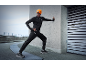 Man in black sportswear and orange beanie with light, stretching outdoors.