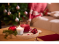 Christmas decoration with red and white candles, baubles, and a Christmas tree in the background.