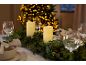 Christmas table decorated with candles, holly and pine garland, and illuminated Christmas tree in background.