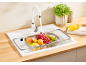 White kitchen faucet with fruit in a colander over a sink and a plant.