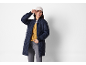 Woman in blue quilted jacket, yellow cardigan, and beige cap.