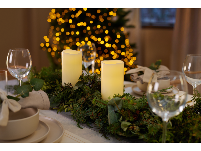 Christmas table decorated with candles, holly and pine garland, and illuminated Christmas tree in background.