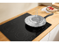 Frying pan with splatter guard on an induction hob in a kitchen.