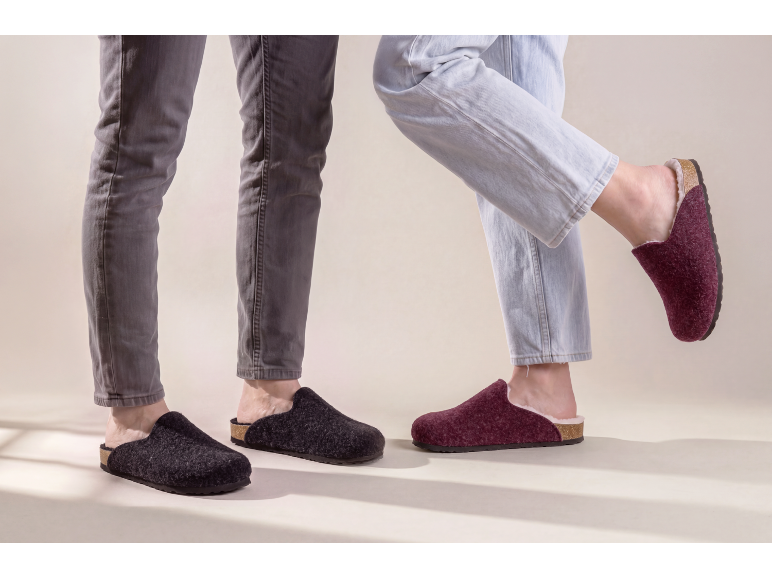 Two pairs of feet in felt slippers, one dark grey and one burgundy.