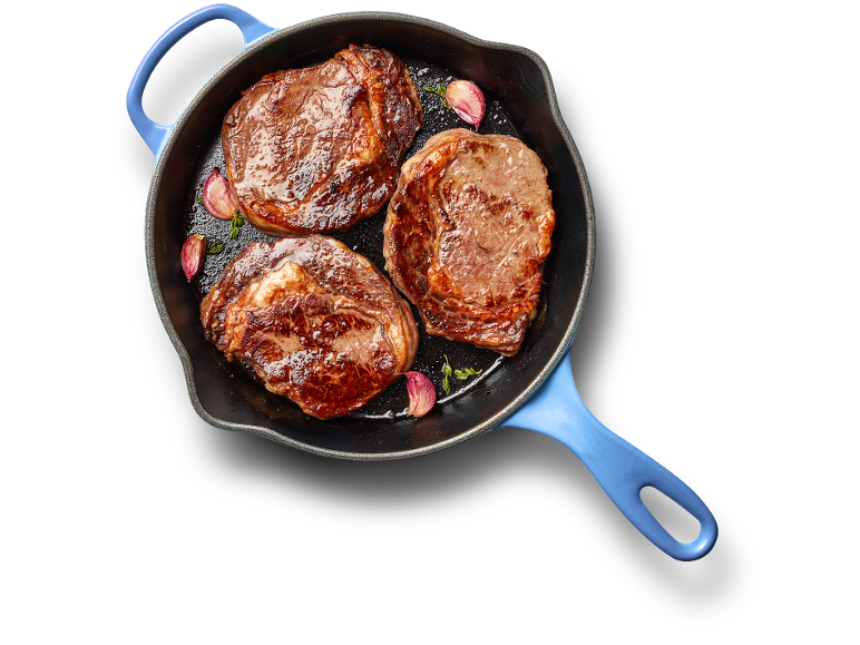 Three juicy steaks cooked in a blue cast iron skillet with garlic and herbs.