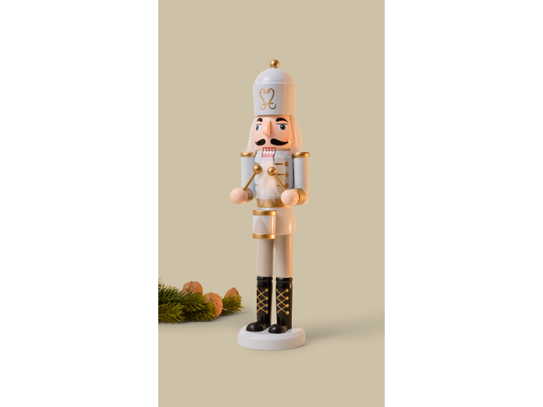 White wooden nutcracker with gold details, fir branches, and walnuts.