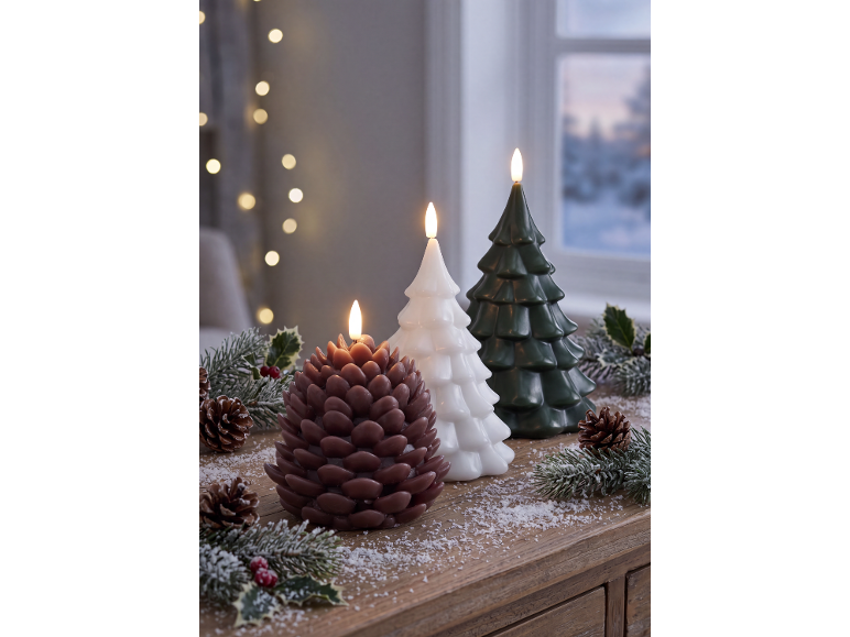 Three lit LED candles shaped like Christmas trees and a pinecone on a snowy wooden table.