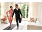 Couple in comfortable tracksuits stretching on yoga mats in a bright living room.
