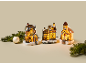 Lit-up Christmas village houses and church with 'Toy Shop' sign and festive decor.