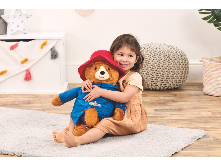 Little girl hugging a large plush bear, sitting on a light rug.
