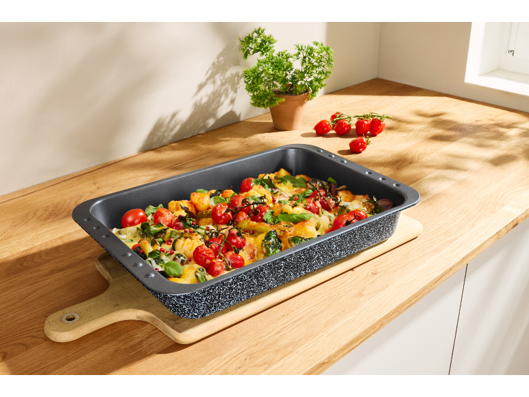 Baking pan with roasted gnocchi, tomatoes, and herbs on a wooden kitchen counter.