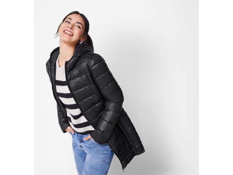 Woman in black quilted jacket, striped sweater, and blue jeans, smiling.