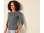 Smiling woman in a long-sleeved top and jeans, leaning against a wall.