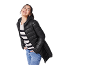 Smiling woman in black puffer jacket, striped sweater, and jeans.