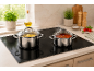 Two stainless steel pots with glass lids on an induction hob, cooking potatoes and sauce.
