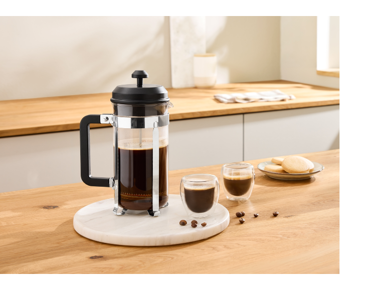 French press with two cups of coffee and cookies on a wooden kitchen counter.