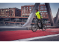 Man in a cycling jacket and helmet riding an e-bike on a red bike path.