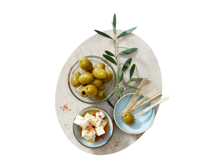 Green olives, feta cheese, and an olive branch on a wooden serving board.