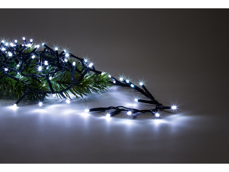 Fir branches with bright white Christmas lights on a grey background.