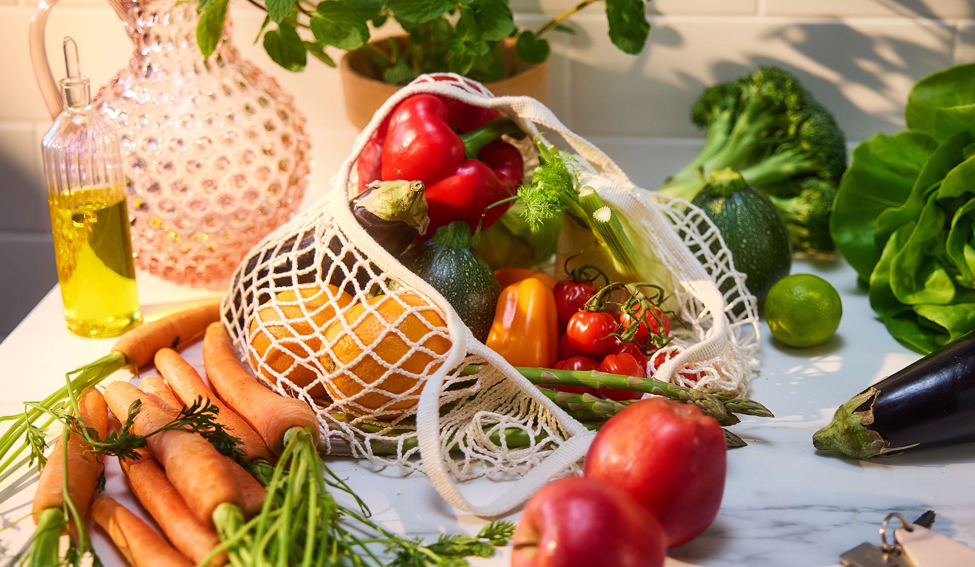 Fresh vegetables and fruits, including bell peppers, oranges, and carrots, in a shopping bag.
