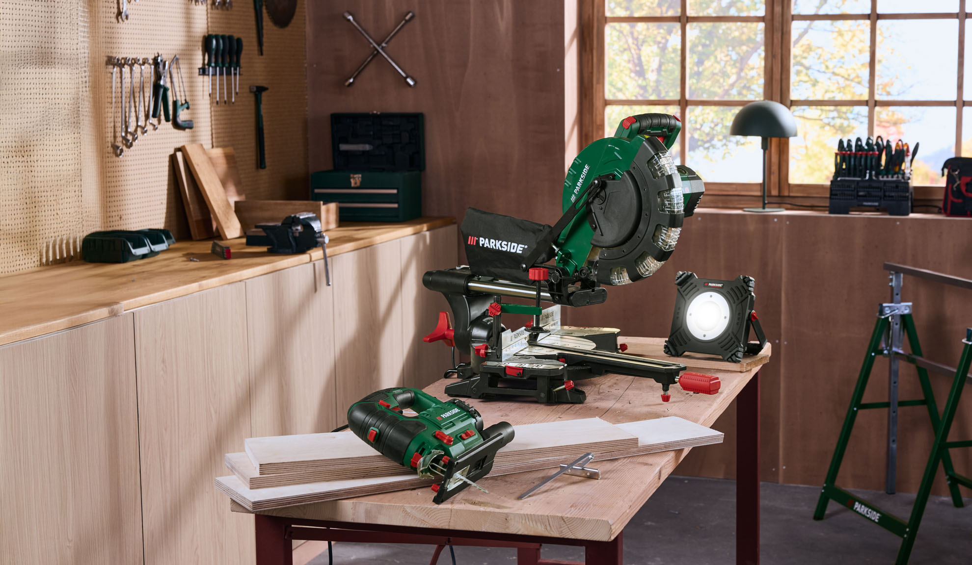 A miter saw, jigsaw, and work light on a workbench in a workshop.