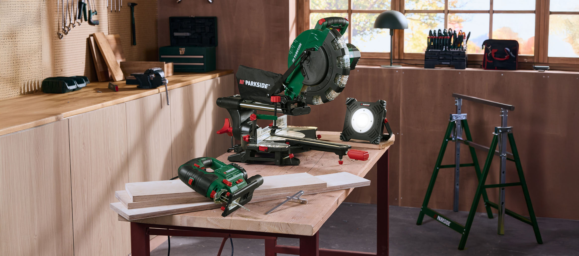 Workshop table with a miter saw, work light, jigsaw, and pieces of wood.